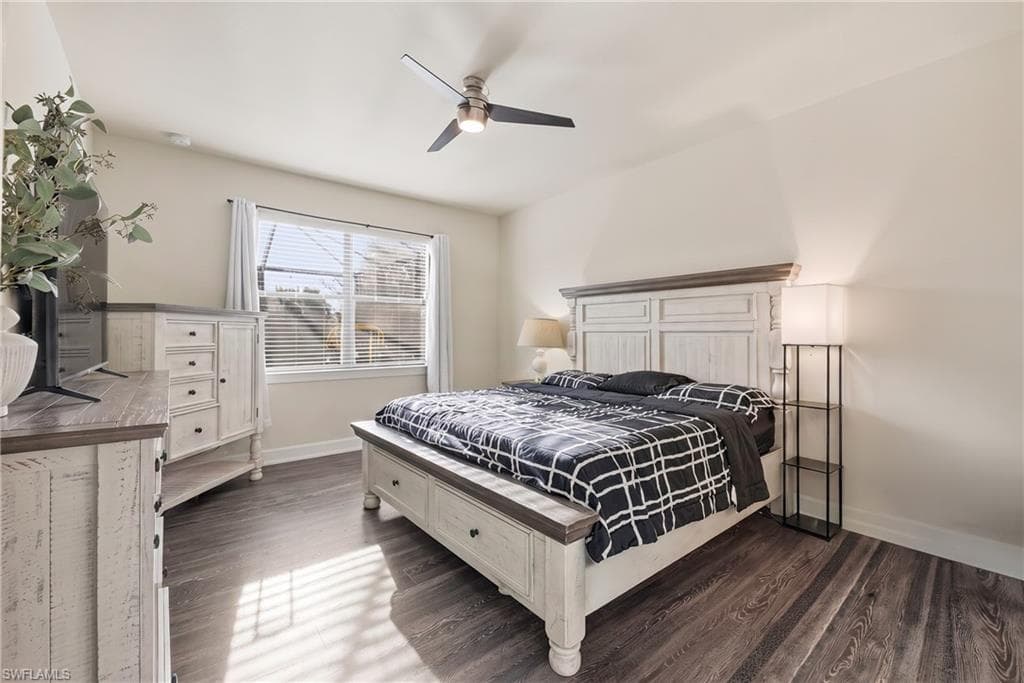 Spacious bedroom featuring a white wood bed frame, coordinating dresser and nightstands with ample storage, dark wood-finish flooring, ceiling fan with integrated lighting, and sliding glass doors providing natural light and access to outdoor space