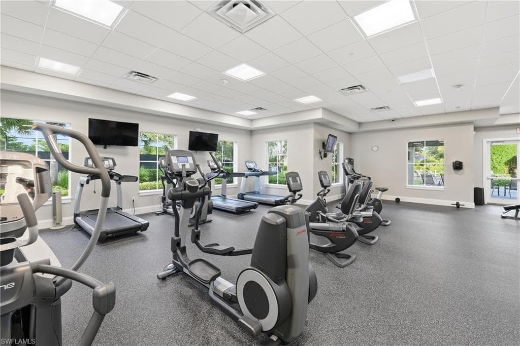 Fitness center featuring cardio equipment, multiple wall-mounted screens, recessed lighting, and large windows