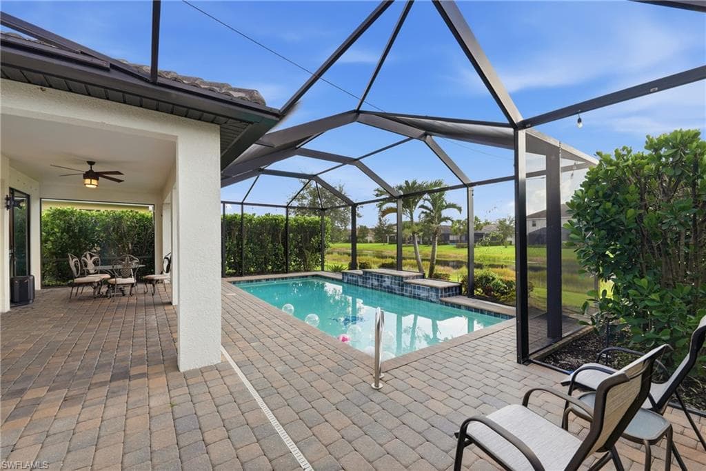 Screened lanai featuring a swimming pool with a waterfall, paver patio, covered outdoor living space with a ceiling fan, and lush landscaping