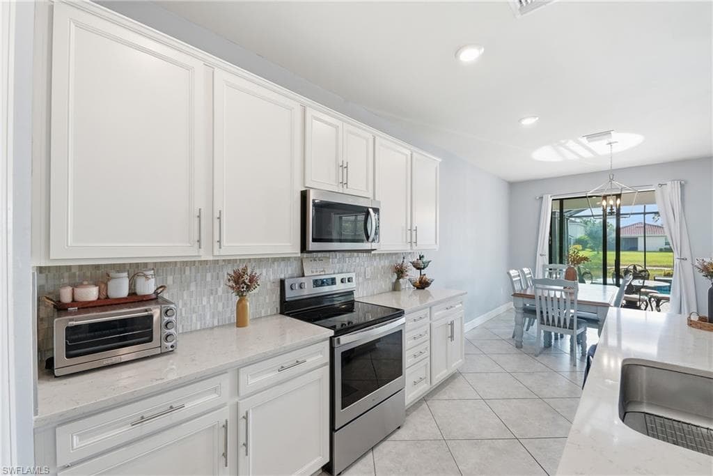 Kitchen featuring white shaker cabinetry, stainless steel appliances, light-toned countertops, and a tile backsplash