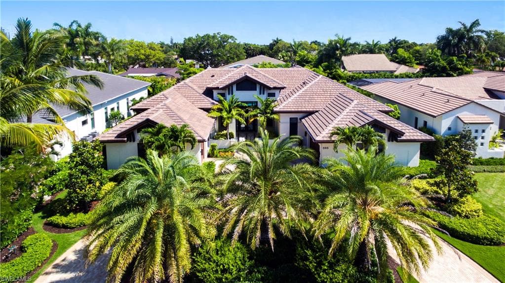 Expansive estate featuring a terracotta tile roof, stucco exterior, lush tropical landscaping with mature palm trees, and a paver driveway
