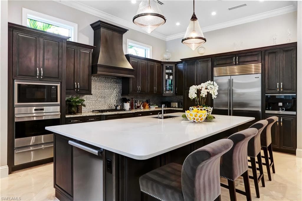 Spacious kitchen featuring dark wood cabinetry, a large center island with a light-toned countertop, and integrated stainless steel appliances including a double oven and refrigerator