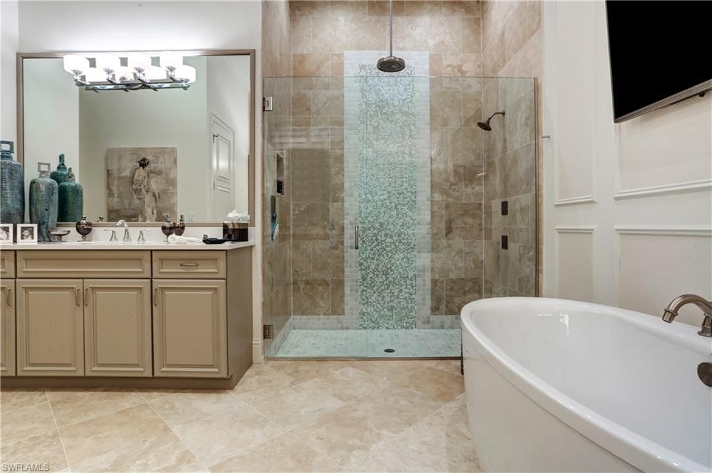 Spacious bathroom featuring a freestanding soaking tub, a walk-in shower with dual shower heads and mosaic tile detailing, a double vanity with a large mirror, and paneled wall trim