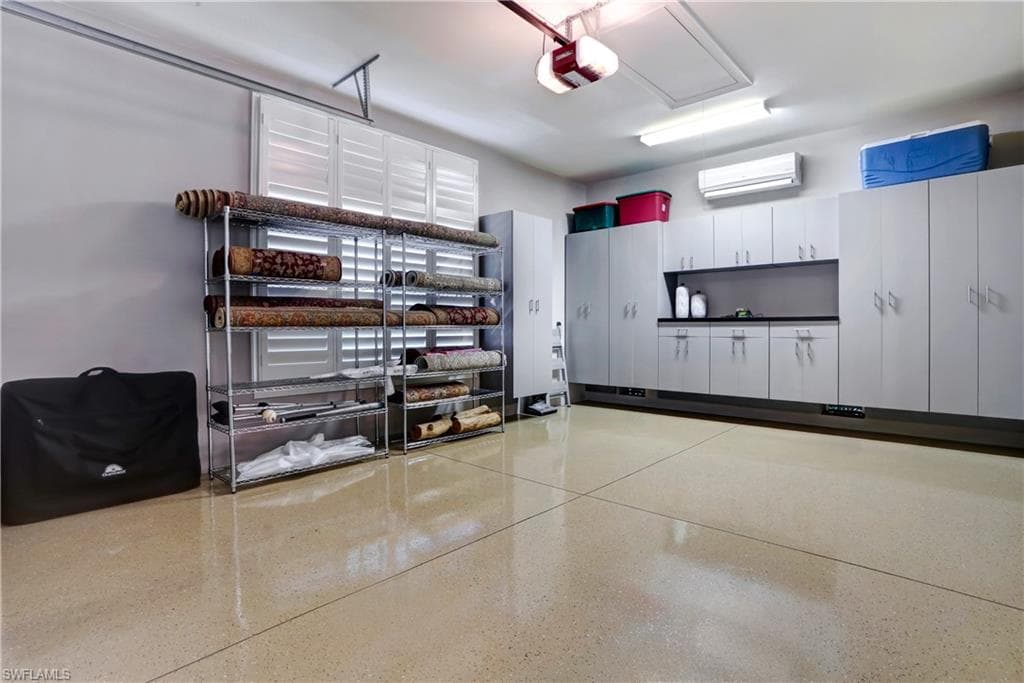 Spacious garage featuring light-toned epoxy flooring, extensive built-in cabinetry with a dark countertop and backsplash, and an overhead lighting system
