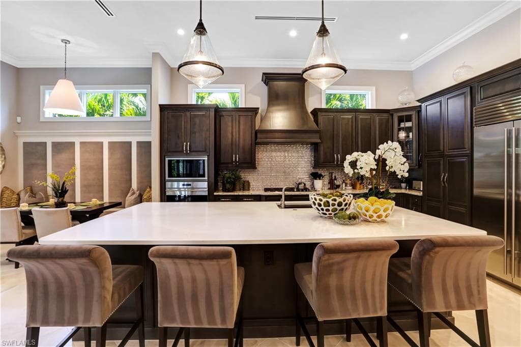 Spacious kitchen featuring a large central island with seating, dark wood cabinetry, stainless steel appliances, and a mosaic tile backsplash