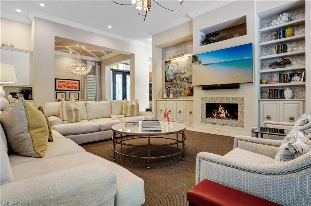 Living area featuring a gas fireplace with a stone surround, built-in shelving, recessed lighting, and crown molding