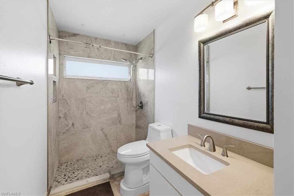 Bathroom featuring a stone-look tiled shower with a pebble floor, horizontal privacy window, a built-in shower niche, and a vanity with an integrated sink and brushed nickel faucet