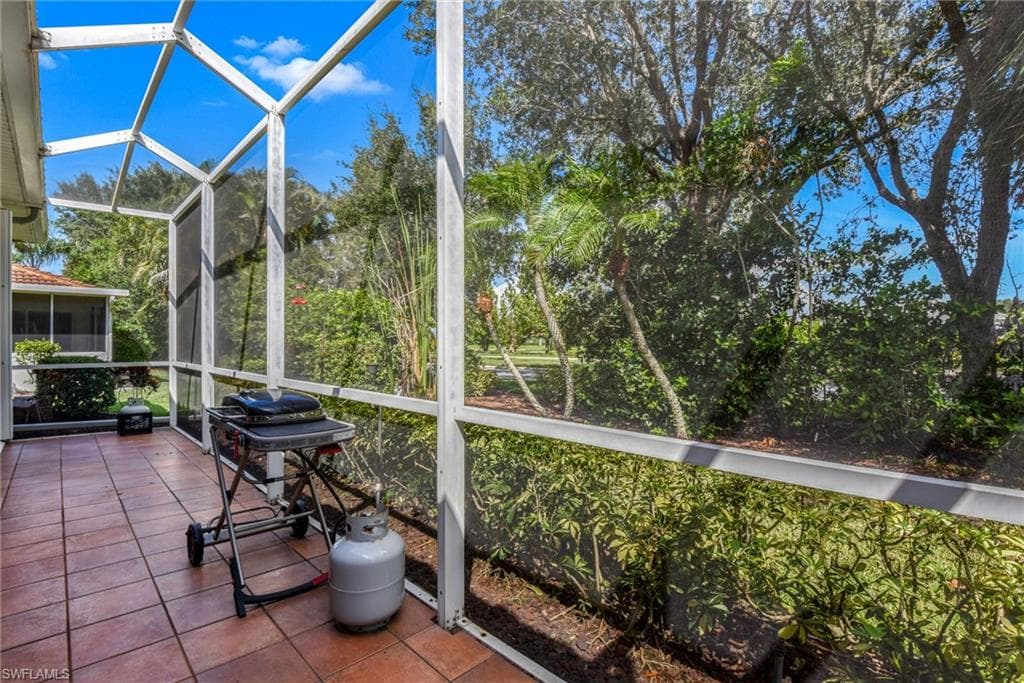 Screened outdoor patio featuring a terracotta tile floor and a lush green backdrop of trees and shrubs