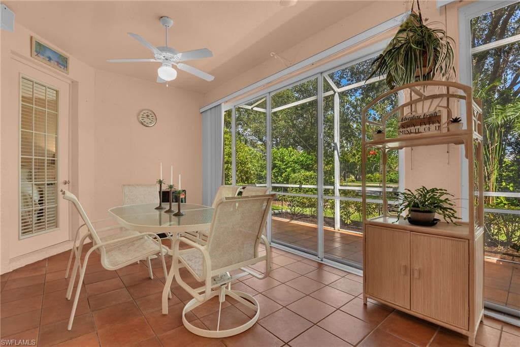 Screened outdoor room featuring terra cotta tile flooring, a ceiling fan, and abundant natural light