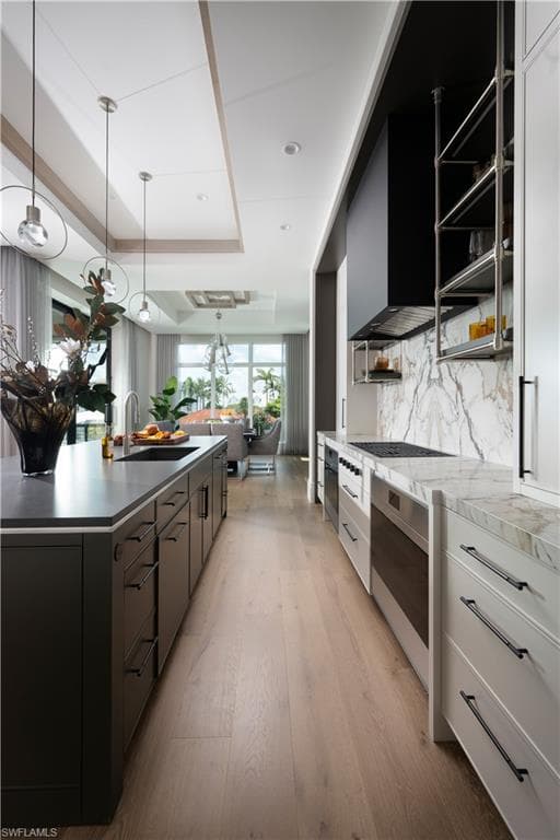 Contemporary kitchen featuring an expansive center island with an undermount sink, pendant lighting, professional-grade appliances, and wood-finish flooring