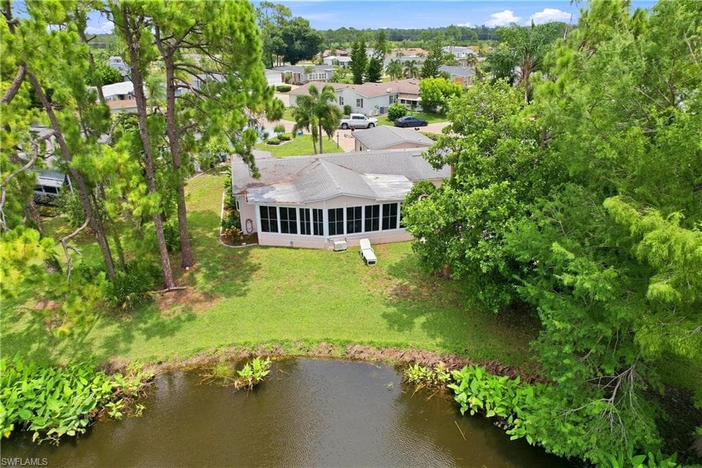 Waterfront property featuring a sunroom, mature trees, and a spacious green lawn