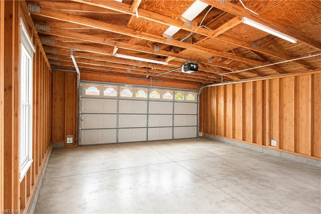 Spacious garage featuring exposed wood framing, a concrete floor, and an automatic garage door with upper window inserts