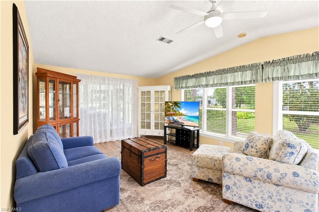 Living area with vaulted ceilings, wood-finish flooring, and multiple windows