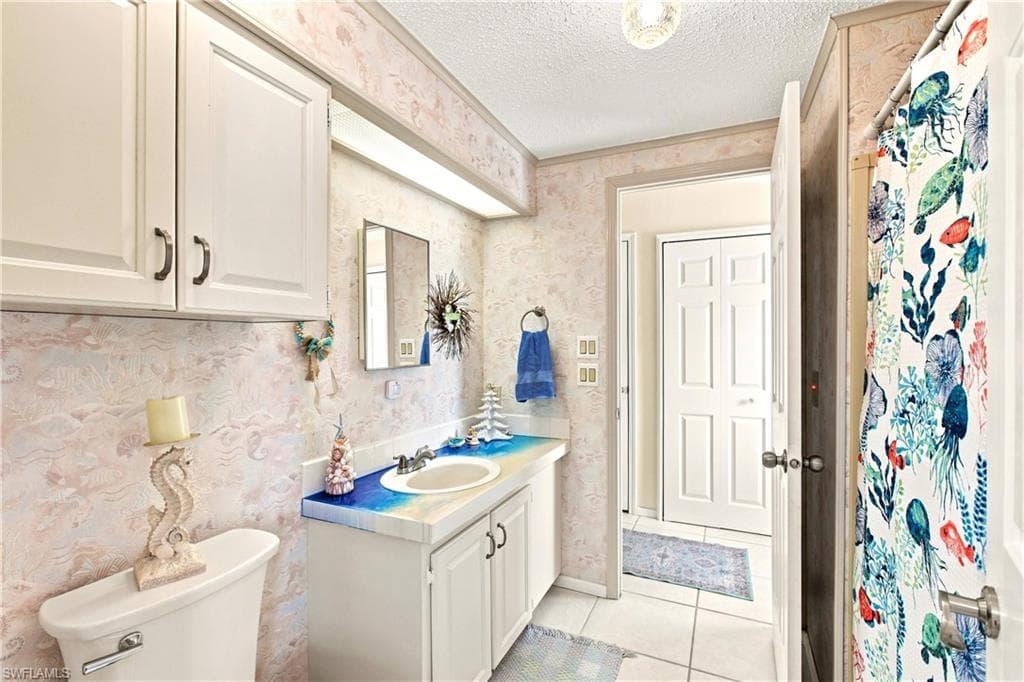 Bathroom featuring white cabinet vanity with integrated sink, white tiled flooring, and a white toilet