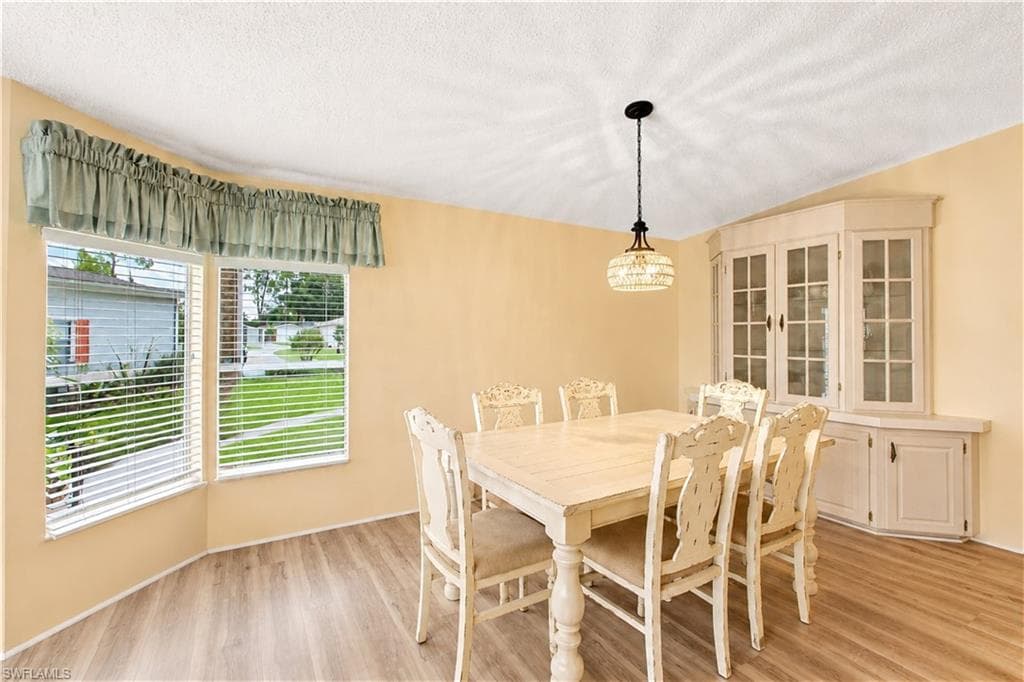 Dining area featuring wood-finish flooring, two large windows with blinds, a corner built-in cabinet with glass doors, and a decorative pendant light fixture