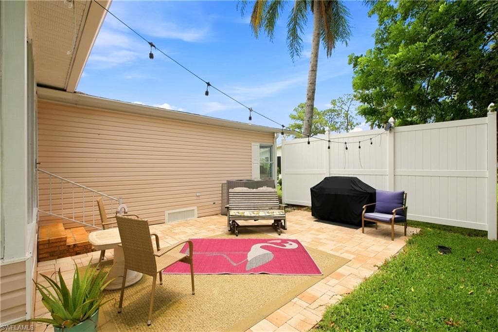 Outdoor patio featuring paver flooring, string lighting, and a white privacy fence