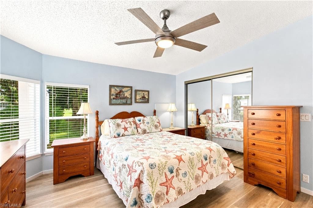 Bedroom featuring wood-finish flooring, a ceiling fan with integrated lighting, a mirrored sliding closet door, and multiple windows with blinds