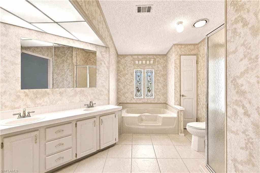 Bathroom featuring a dual vanity with integrated sinks, a garden tub, a walk-in shower with textured glass, decorative stained-glass windows, and neutral tile flooring