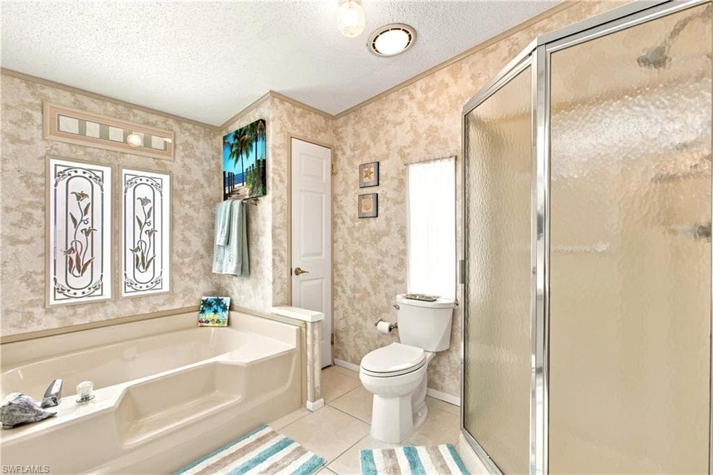 Bathroom featuring a built-in tub, a separate glass-enclosed shower, a toilet, and light-toned wall finishes