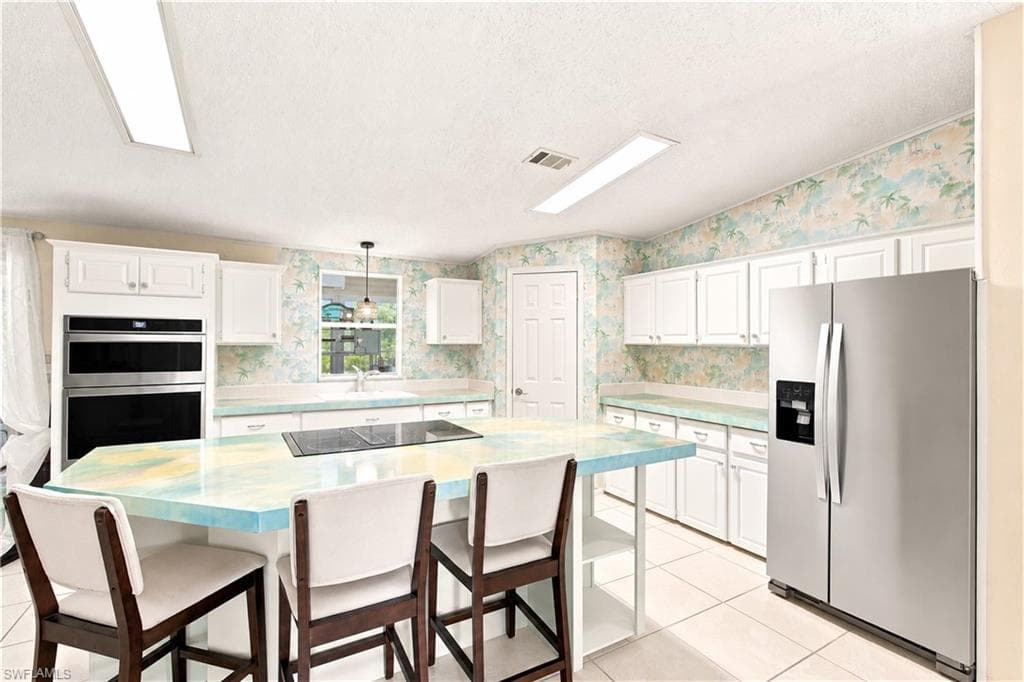 Kitchen featuring a central island with integrated cooktop, white cabinetry, double wall oven, stainless steel refrigerator, and tiled flooring