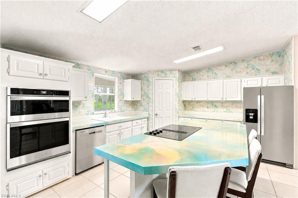 Kitchen featuring a central island with an integrated cooktop, double wall ovens, stainless steel appliances, white cabinetry, and tiled flooring
