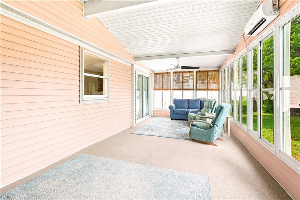 Enclosed sunroom featuring a ceiling fan, wall-mounted air conditioning unit, light-toned carpet flooring, and numerous windows