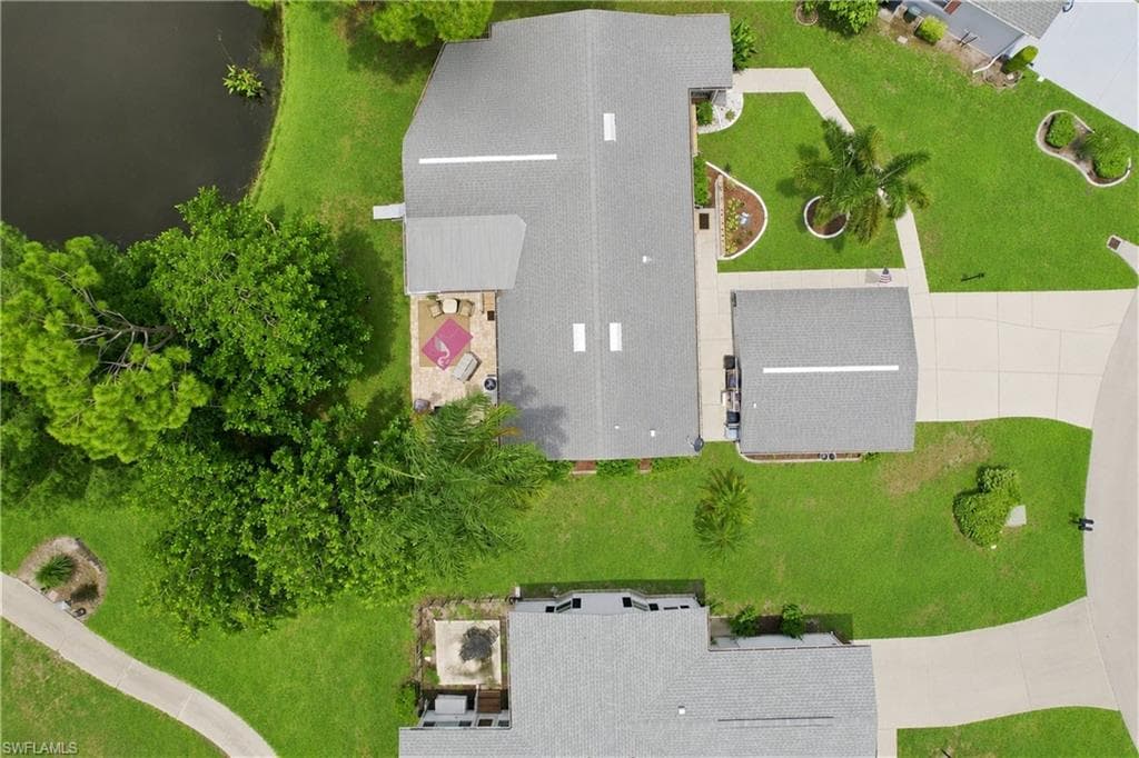 Aerial perspective highlighting a residential property with a shingle roof and an attached covered patio featuring stone pavers