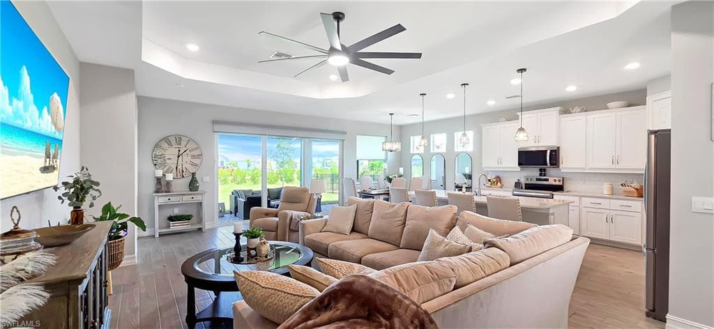 Bright living area featuring plank ceramic floors, tray ceiling, and a modern ceiling fan