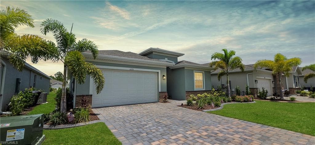 Contemporary stucco exterior featuring a two-car garage, paver driveway, mature palm trees, and established landscaping