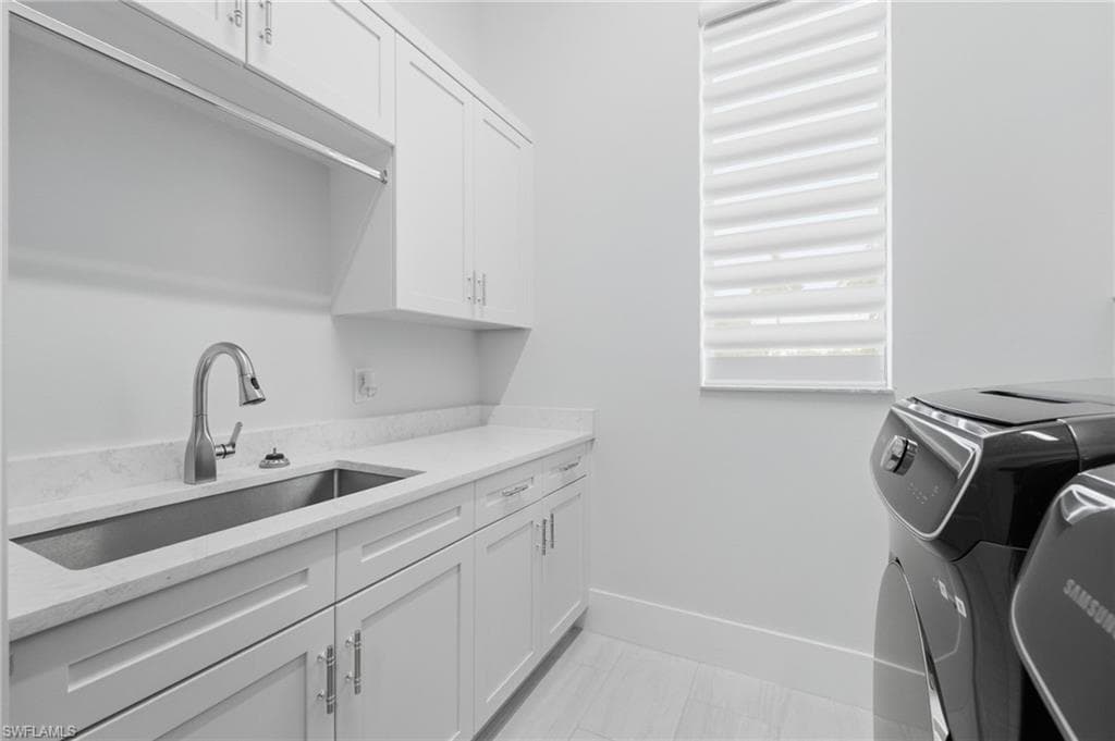 The thoughtfully appointed laundry room is filled with natural light and features a washer and dryer with washer offering built-in intimates space, additional cabinetry, a utility sink, and convenient hanging space for effortless organization.