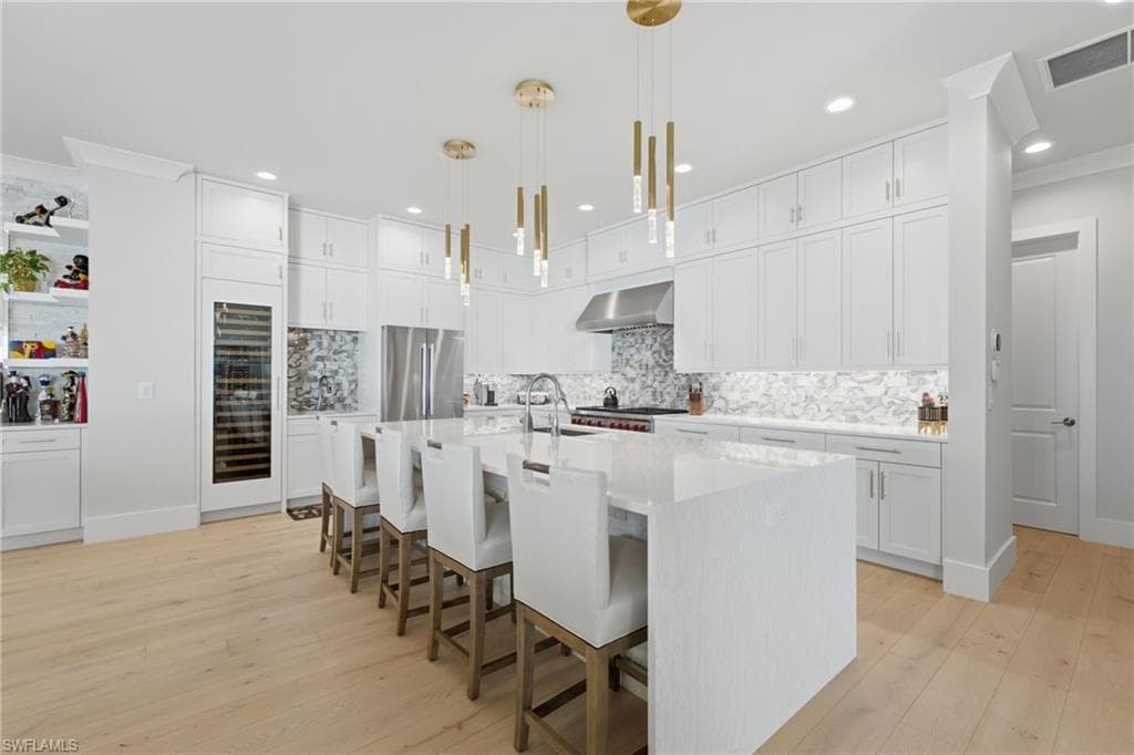 The one-of-a-kind chef’s kitchen is a study in refined luxury, showcasing a dramatic waterfall-edge quartz island, custom wood cabinetry extending to the ceiling, a striking designer backsplash, and bespoke lighting. A six-burner Wolf range with integrated grill is complemented by dual Wolf ovens, Bosch refrigeration, dual Franke sinks, and an additional 100+ bottle wine cooler, creating an exceptional culinary and entertaining experience.