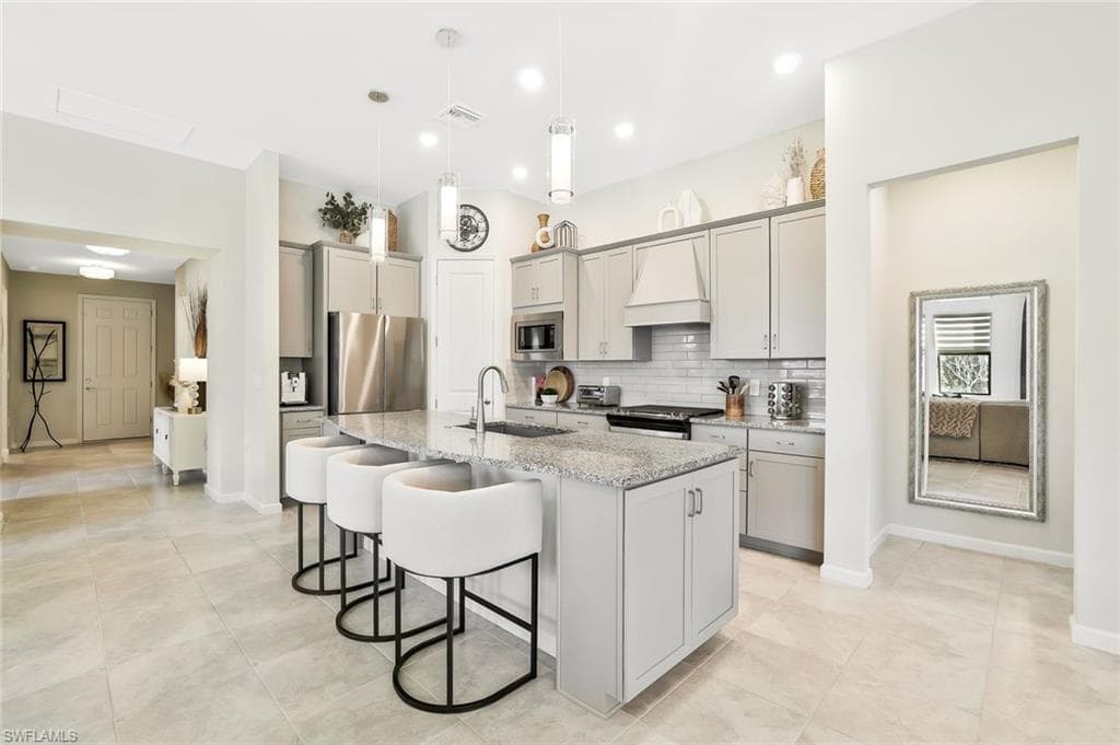 Kitchen featuring a central island with countertop seating, light gray cabinetry, stainless steel appliances, a subway tile backsplash, and recessed lighting