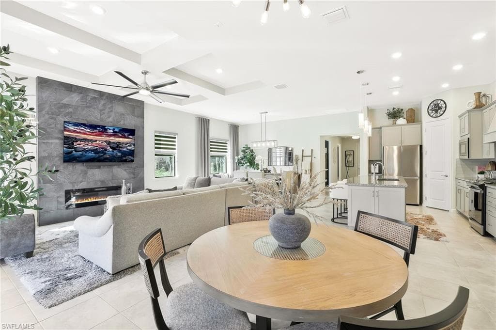 Open-concept living space featuring a modern fireplace with a full-height stone-look surround, tray ceiling with recessed lighting, and a kitchen with stainless steel appliances and a center island