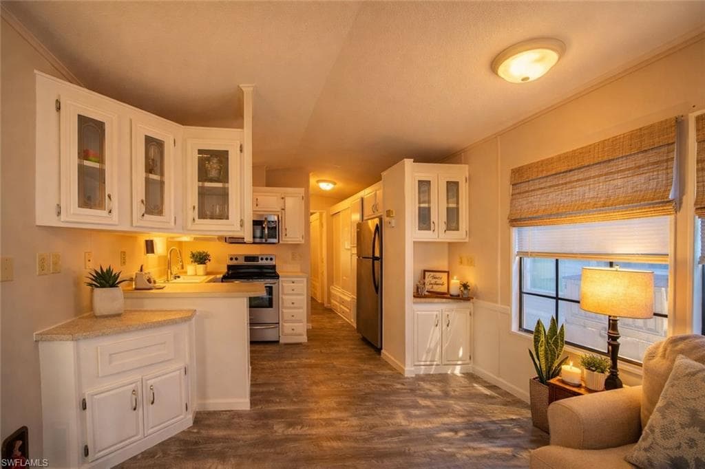 Kitchen with glass fronted cabinets, white cabinetry, light countertops, stainless steel appliances, and dark wood-style floors