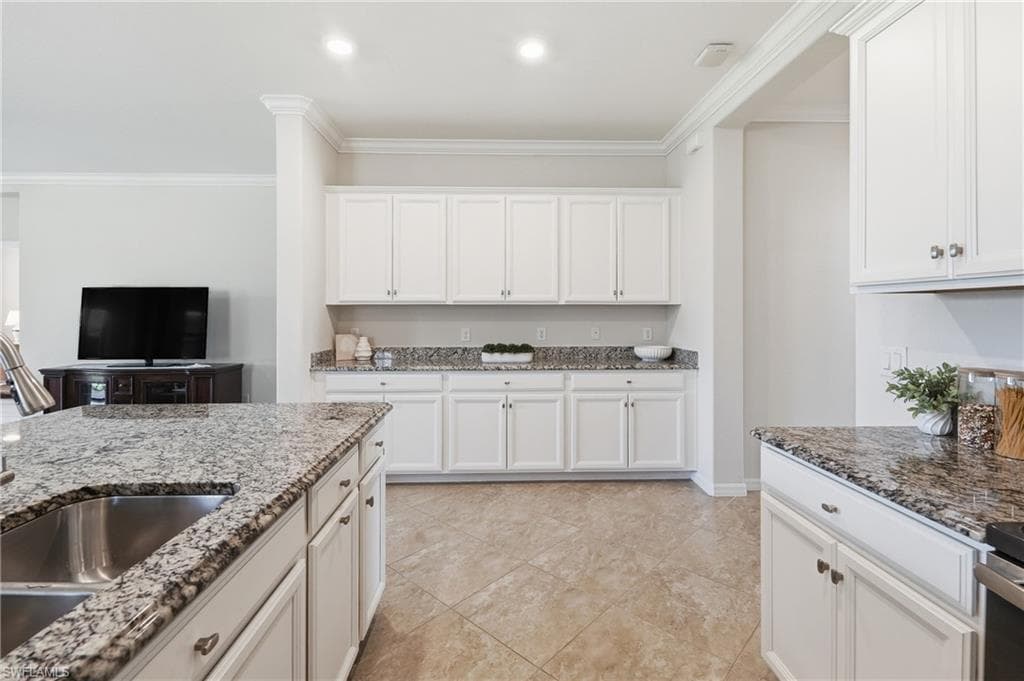 Kitchen featuring a large island with an undermount stainless steel sink, extensive white cabinetry, speckled stone countertops, tiled flooring, and recessed lighting