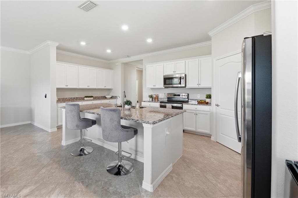 Modern kitchen featuring a central island with a granite countertop, white cabinetry, and stainless steel appliances