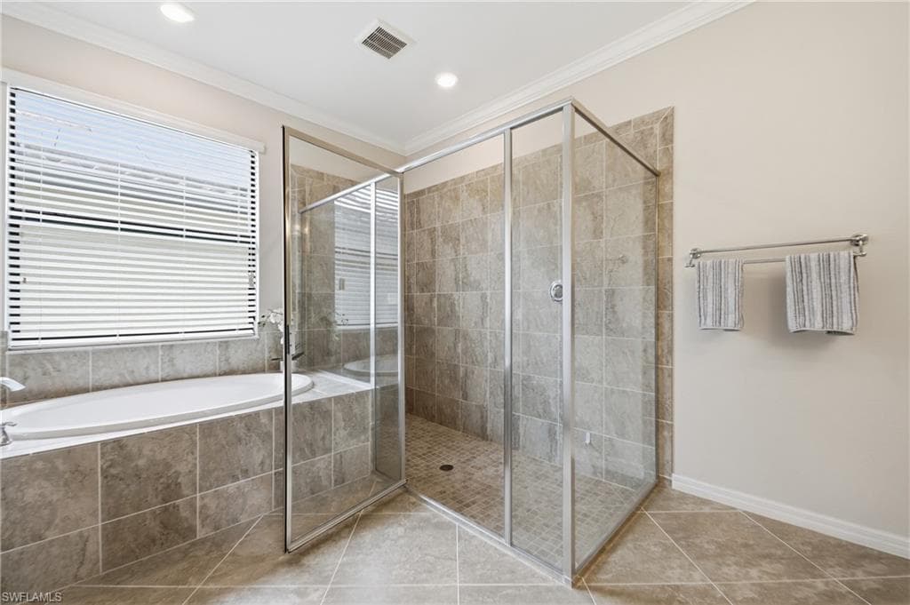 Spacious bathroom featuring a glass-enclosed shower, a large soaking tub with a tiled surround, and extensive tiled flooring