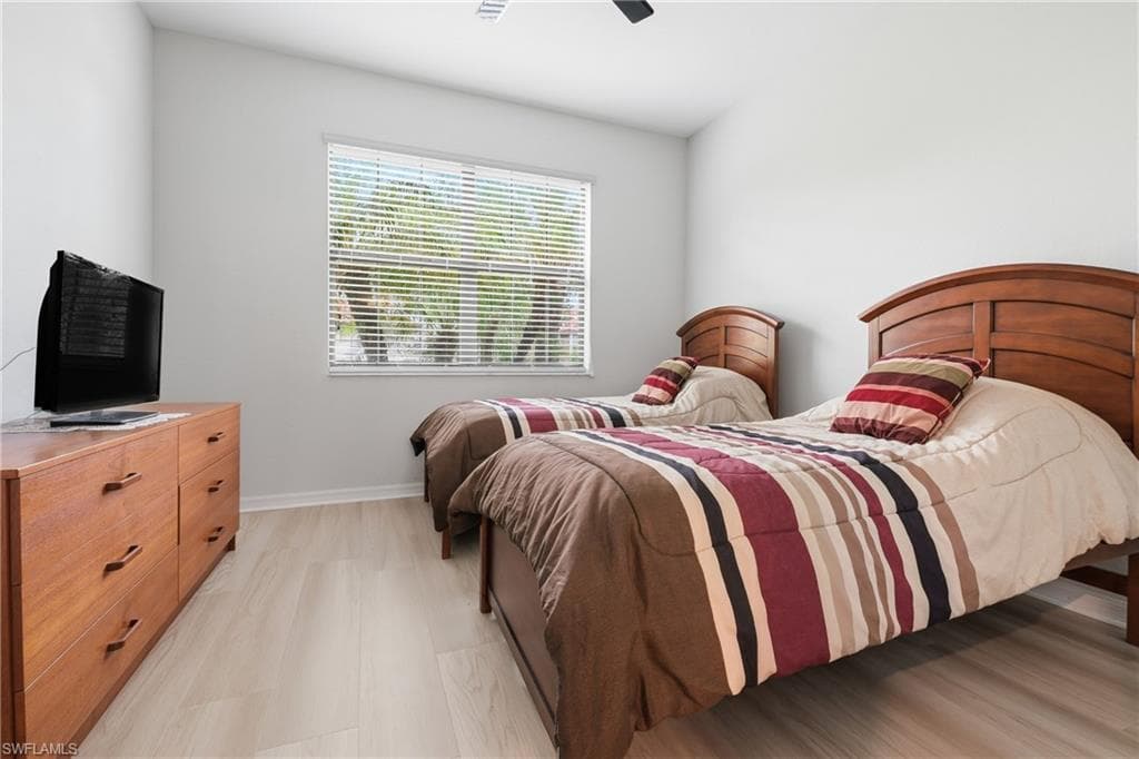 Bedroom featuring light wood-finish flooring, a large window with horizontal blinds, and a ceiling fan