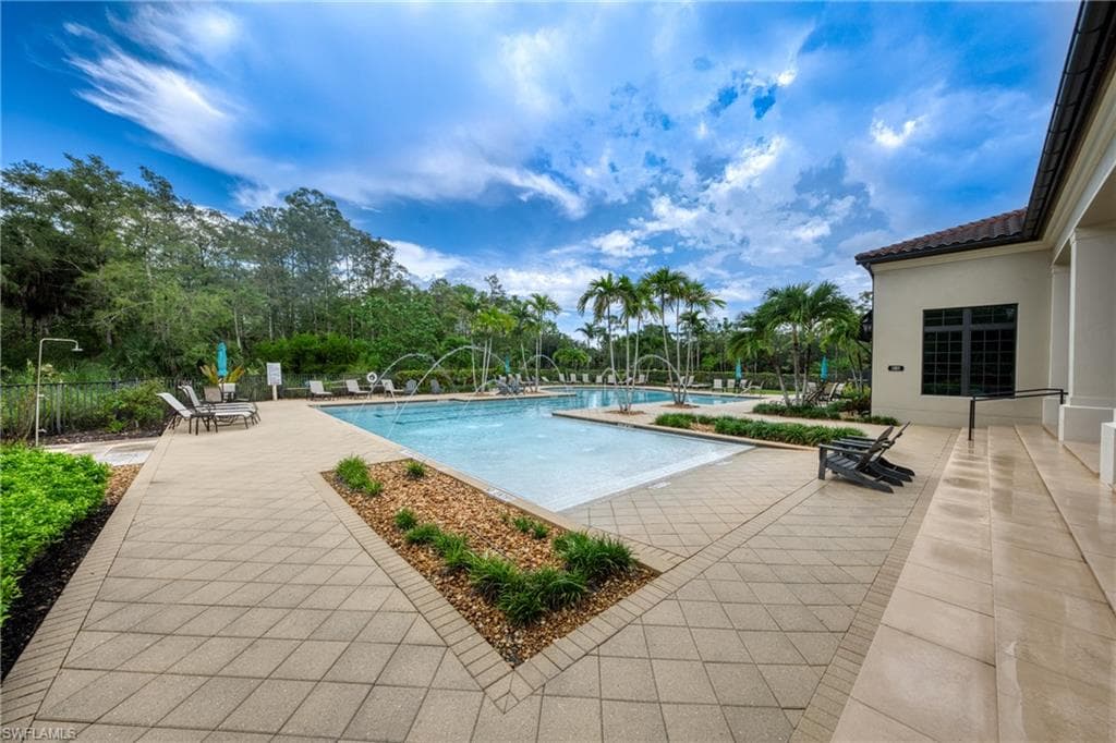 Expansive swimming pool with water features, surrounded by a paver patio and mature palm trees