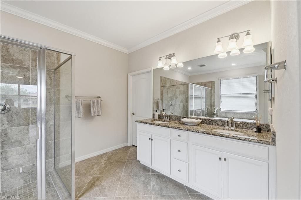 Bathroom featuring a glass-enclosed shower with tile surround, dual vanity with white cabinetry, granite countertop, and tile flooring