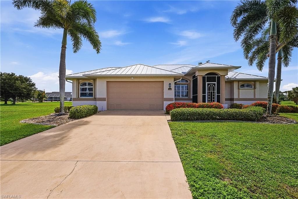 Elegant single-story residence featuring a stucco exterior with metal roof, dual royal palm landscaping, and a concrete driveway approach