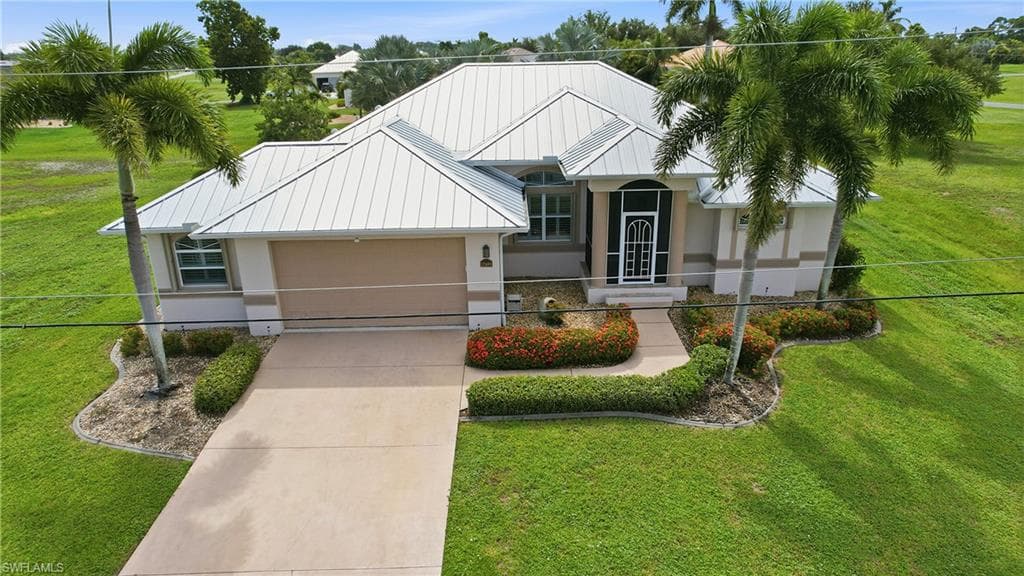 Elegant contemporary residence featuring a metal roof with clean geometric lines, two-car garage with paneled door, and mature landscaping including palm trees and manicured foundation plantings