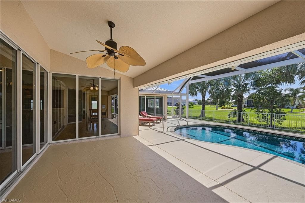 Screened lanai with pool featuring expansive under-truss seating area, textured concrete patio, and a ceiling fan
