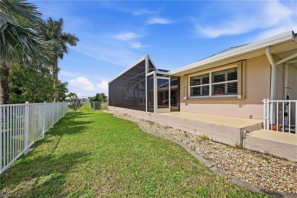 Exterior stucco finish with a screened patio enclosure, elevated concrete patio, and a white aluminum fence bordering a grass lawn