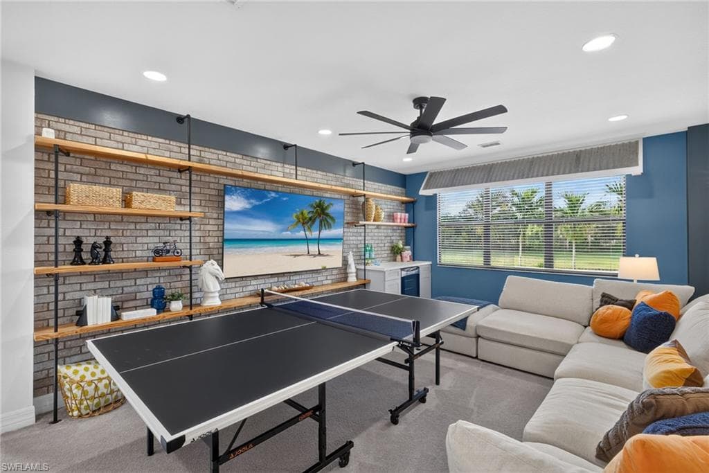 Recreational loft featuring a brick accent wall with wood shelving, large windows with blinds, a built-in wet bar, and recessed lighting