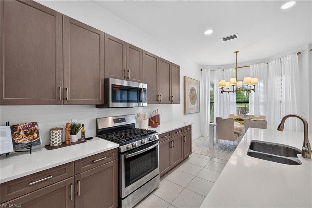 Galley kitchen featuring stainless steel appliances, solid surface countertops, extensive cabinetry, and tile flooring