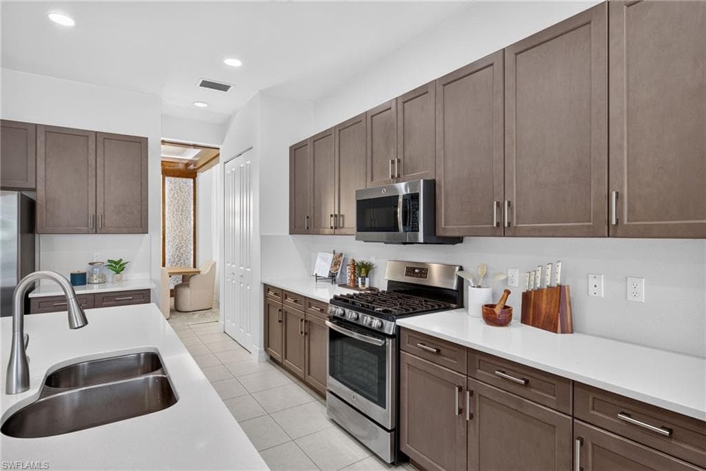 Modern kitchen featuring light-toned cabinetry, stainless steel appliances, a dual basin sink, white countertops, and tile flooring