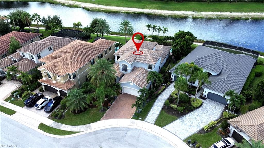 Waterfront property with a tile roof, paver driveway, and mature landscaping