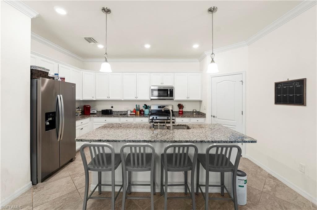 Kitchen with granite countertops, a center island with double-basin sink, white cabinetry, stainless steel appliances, and pendant lighting. Open to the living and dining areas.