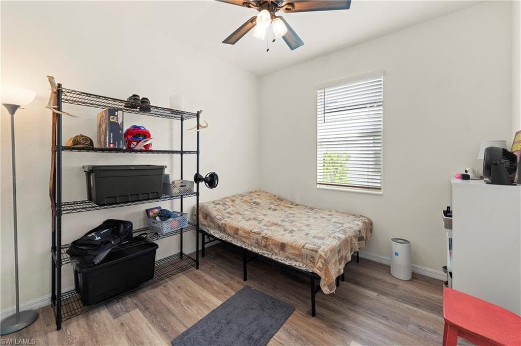 Room featuring wood-finish flooring, white baseboards, a window with horizontal blinds, and a ceiling fan with light fixture